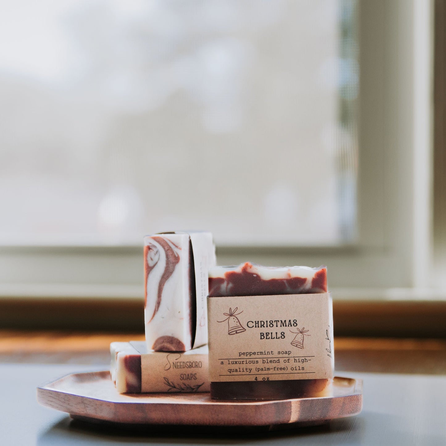 Three soap bars on a wooden tray with a blurred window background